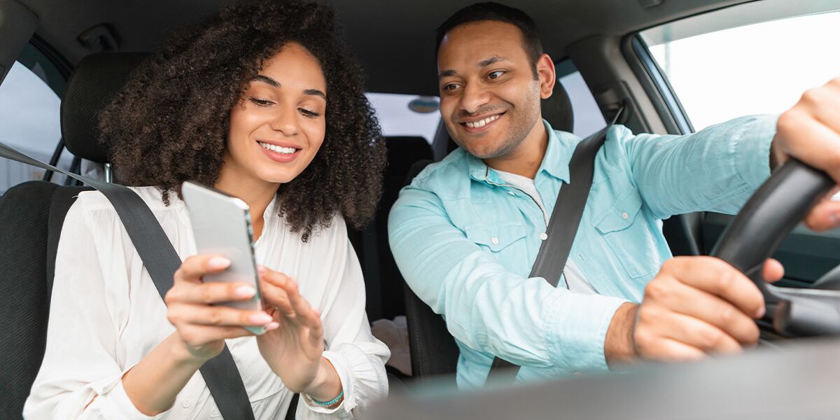 Casal sorrindo dentro de um carro olhando para o celular