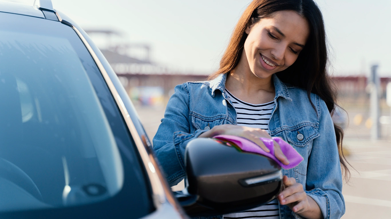 Mulher limpando o espelho de um carro