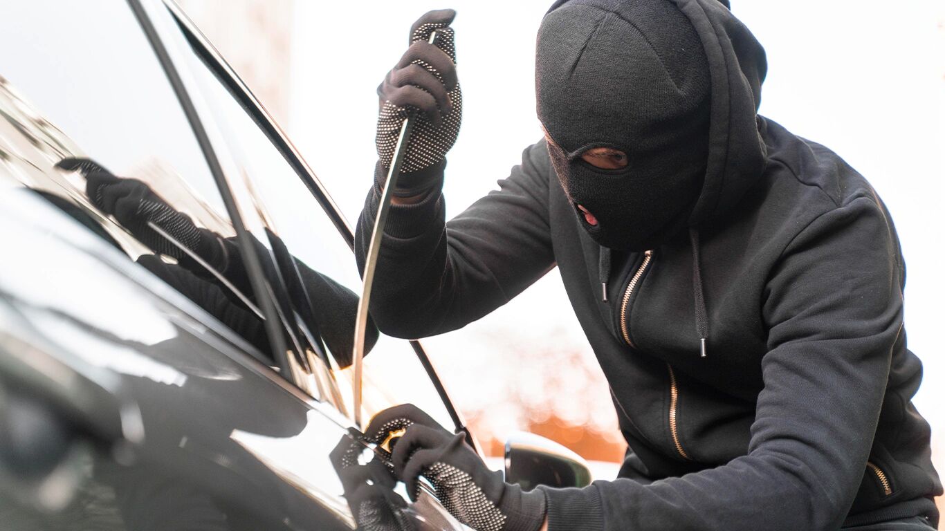 Homem de capuz tentando roubar um carro.